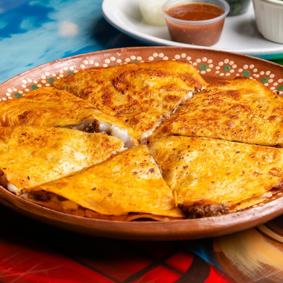 Golden-brown Magueys Mexican Restaurant quesadillas, filled with meat and melted cheese, served on a decorative plate.