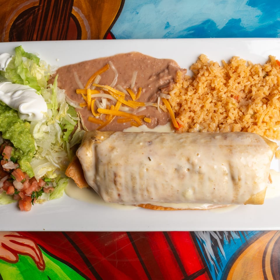 A Magueys Mexican Restaurant chimichanga covered in white sauce, with rice, beans, and salad.